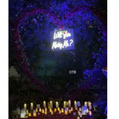 A wide view of an enchanting outdoor proposal setting at night. I used a large heart-shaped floral arrangement, a neon sign, and dozens of LED candles to create a warm, magical glow.