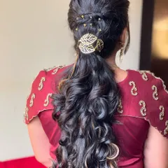 A modern and chic ponytail hairstyle with voluminous curls. This look is perfect for a reception or party, and is accented with a delicate, leaf-patterned hair clip.