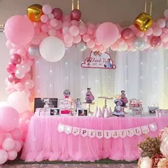 A sweet and personal pink-themed decoration. This setup features a beautiful balloon garland over a fairy-lit curtain and includes framed photos of the birthday girl on the main table.
