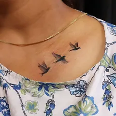 Three small birds in flight on the collarbone, symbolizing freedom and journey. The clean silhouettes make for a timeless and elegant minimalist tattoo.