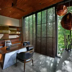 Sunlight filters through wooden blinds into the study, creating a calm and productive atmosphere. The design balances privacy with a strong visual connection to the lush garden just beyond the glass walls.
