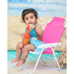 A cute close-up of the baby girl on her pink beach chair, curiously inspecting her toy bottle. These little moments of discovery are what make baby photoshoots so special.