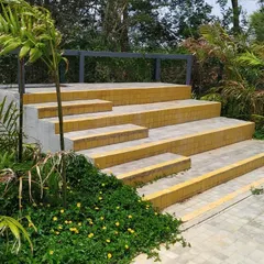 These yellow-tiled steps are nearing completion, nestled within lush green foliage. This detail shows how simple, colorful materials can create inviting transitions within the landscape of a residential layout.
