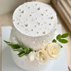 An overhead view showing the delicate pearl work on the top tier of this elegant white cake. The placement of the fresh roses adds a touch of natural beauty.