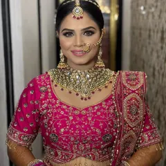 A happy, smiling portrait of the bride. The makeup features a classic smokey eye and a soft pink lip, perfectly complementing her vibrant pink outfit and heavy kundan jewelry.