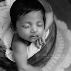 A two-month-old baby sleeps in a wooden bucket, captured in timeless black and white. The angle and the baby's slight smirk create a beautiful and artistic portrait.