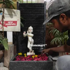 An artisan carefully adds flower petals to the water of the Kanha Ji fountain, preparing it for display.