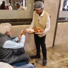 I ensure all guests are catered to with care and respect. A member of my staff is seen here serving appetizers to a senior guest, ensuring a comfortable experience for everyone.