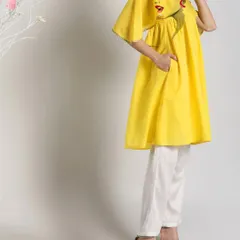 A full-length view of a bright yellow hand-painted kurti paired with white pants. The pop-art style face on the shoulder adds a modern and fashionable twist to the traditional silhouette.