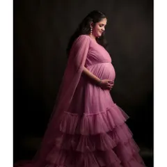 A side profile showcasing the beautiful silhouette of pregnancy in our flowing pink maternity gown. The studio lighting is set to create a soft, classic portrait.