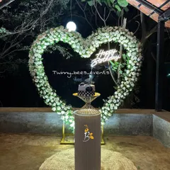 An elegant and romantic birthday or anniversary setup. This features a heart-shaped arch made of white flowers with a "Happy Birthday" neon sign, perfect for a surprise celebration at night.