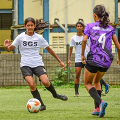 An SG5 player skillfully maneuvering past a defender in the MFA YPL Junior Girls League. The focus and technique on display are a result of dedicated training.