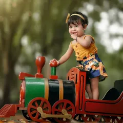 All aboard for a fun adventure. This little girl is so excited to be the conductor of her own toy train in this whimsical outdoor photoshoot.