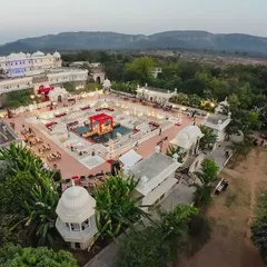 An aerial shot capturing the spectacular scale of the wedding at Alsisar Nahargarh's Hathi Kund. The vibrant red floral mandap sits like a jewel in the water, creating a 360-degree visual spectacle for a truly regal experience.