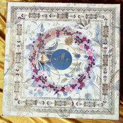 A top-down view of this exquisite invitation box, featuring a stunning floral wreath of pink and magenta blossoms. The design is layered over a subtle, classic background, with a central monogram that makes it uniquely yours.