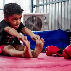 A young warrior takes a moment to stretch after a tough session. We teach kids the importance of flexibility and recovery, preparing them for a professional career in combat sports if they choose.