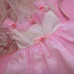 A fairy-tale dream in soft pink. This dress features a delicate lace bodice and layers of sheer fabric, adorned with tiny rosebuds and organza bows on the shoulders for an ethereal, magical look.