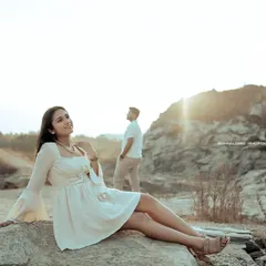 The bride-to-be basks in the golden hour light, while her partner stands in the background. This creative composition tells a story of love and anticipation.