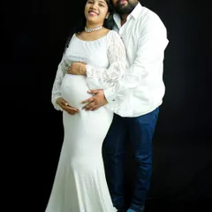 A classic and elegant couple portrait. The mom-to-be wears a beautiful white lace gown while her partner stands with her, both sharing a happy moment. This was shot against a simple black backdrop to make them stand out.