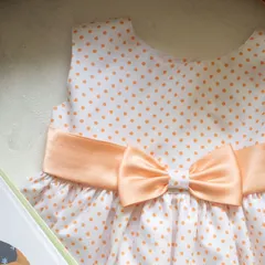 A classic combination of peach polka dots on a white background. The wide satin bow at the waist adds a touch of elegance and defines the silhouette beautifully.
