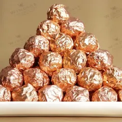 A pyramid of my signature NOCOCHOCO hazelnut truffles, each wrapped in rose gold foil. These are made with fresh toasted hazelnuts, crunchy wafer, and creamy milk chocolate for an irresistible texture.