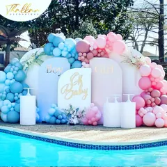 A beautiful "Oh Baby" gender reveal or baby shower setup by the pool. The decor uses pink and blue balloon arches against a clean white backdrop for a modern and chic look.