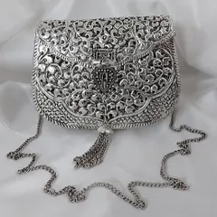 This intricately carved silver clutch is a masterpiece of traditional craftsmanship. With its delicate tassel and chain strap, it’s the perfect heirloom accessory for any grand occasion.