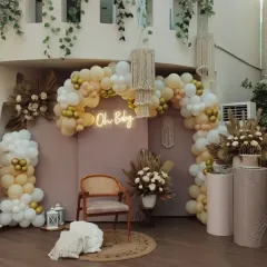 A wider shot of the boho baby shower decor, showing the full balloon arch and the cozy seating area with a jute rug and wooden chair.