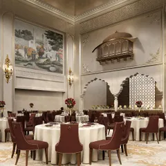 We believe luxury is in the details. This view of a grand banquet hall interior showcases our blend of Rajasthani and Islamic architectural elements, featuring a traditional jharokha, custom maroon seating, and intricate wall murals to create a regal atmosphere for any celebration.