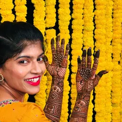 The beautiful bride Sahana, with a smile as bright as her yellow outfit and the marigold backdrop, peeking over her freshly done peacock mehendi.