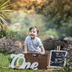 A happy birthday boy in the great outdoors. The natural light and greenery provide a perfect backdrop for his joyful first birthday photos.