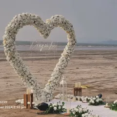For a breathtaking beach proposal, I designed this large heart-shaped arch of white flowers right on the sand, complete with lanterns and a clear acrylic sign for a personal message.