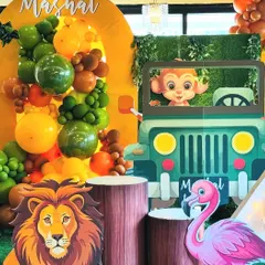 A close-up of the safari jeep prop, where a cute monkey character peeks out, ready for a photo opportunity. The scene is detailed with a lush green foliage backdrop and a vibrant balloon arrangement, highlighting the fun and interactive elements of our jungle theme.