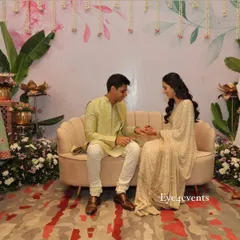 A happy couple sharing a moment during their ring ceremony. They are seated in front of our custom-designed pastel backdrop, which features delicate floral illustrations and hanging flower strings.