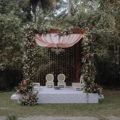 An elegant and romantic mandap for an outdoor wedding, featuring a cascade of flowers and a soft pink canopy set against a lush green backdrop at the Taj West End.