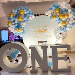 Large "ONE" letters are a popular and impactful prop for first birthday parties. This setup pairs them with a custom-printed backdrop and a blue and gold balloon arrangement.