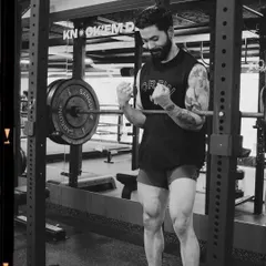 A member celebrates a good lift in the power rack. The black and white film style captures the raw, focused energy of our training floor.