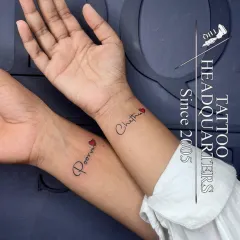A matching couple's tattoo, with the names "Poorni" and "Chathu" inked on their respective wrists, each adorned with a small red heart.