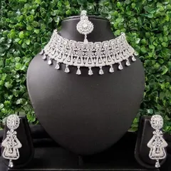 For the modern bride who loves to sparkle, this complete American diamond necklace set is a perfect choice for a reception or cocktail event. It includes a choker, matching earrings, and a delicate maang tikka.