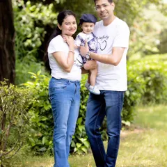 A full-length portrait of a family enjoying their time together in a lush green park. Their coordinated white and denim outfits work perfectly for a casual and candid family photoshoot.