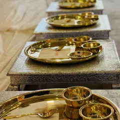 The Royal Thali setup on intricately carved silver chowkis. This combination of gold and silver adds a luxurious feel to the traditional seated dining experience.