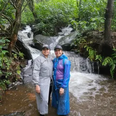 Two friends enjoying a stream crossing on the Netravati trek, well-prepared for the monsoon with their raincoats. The trail is filled with these fun little challenges.