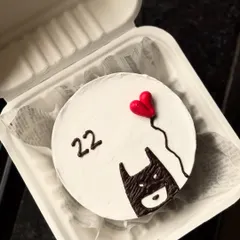 A minimalist and cool Batman-themed bento cake. This design features the Batman symbol holding a red heart-shaped balloon, celebrating a 22nd birthday.