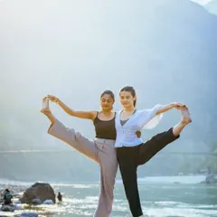 Finding balance together. This partner pose, set against the serene backdrop of Rishikesh, showcases the harmony and stability that can be achieved when you practice with someone else.