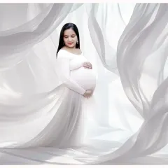 An angelic solo portrait in a flowing white gown. The sheer white fabric drapes around the mother-to-be, creating a soft, dreamy, and ethereal look.