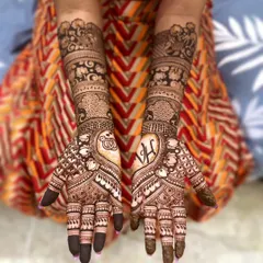 A complete view of a beautiful, symmetrical engagement henna design. The palms feature the couple's initials, 'V' and 'H', woven into a heart shape, while the forearms are decorated with intricate floral and geometric patterns.