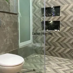 A modern bathroom with a unique chevron-patterned tile on the floor and shower wall. The glass partition and built-in niches create a sleek and functional shower area.