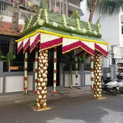 A unique chapra design with pillars made from stacked coconuts painted gold. The roof is decorated with red and white flower garlands, creating a rich and festive look.