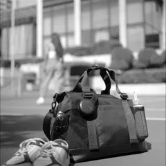 An atmospheric, black-and-white product shot for Lino Perros. Placing the gym bag, shoes, and accessories in the foreground with the model blurred in the back creates a lifestyle context while keeping the product as the hero.