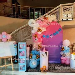 A grand baby shower setup by a staircase. The decor includes pink and blue balloons, butterfly accents, 'BABY' blocks, and a large 'Oh Baby' sign.